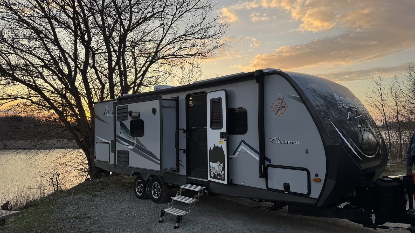 Coachmen Apex travel trailer parked by a lake at sunset